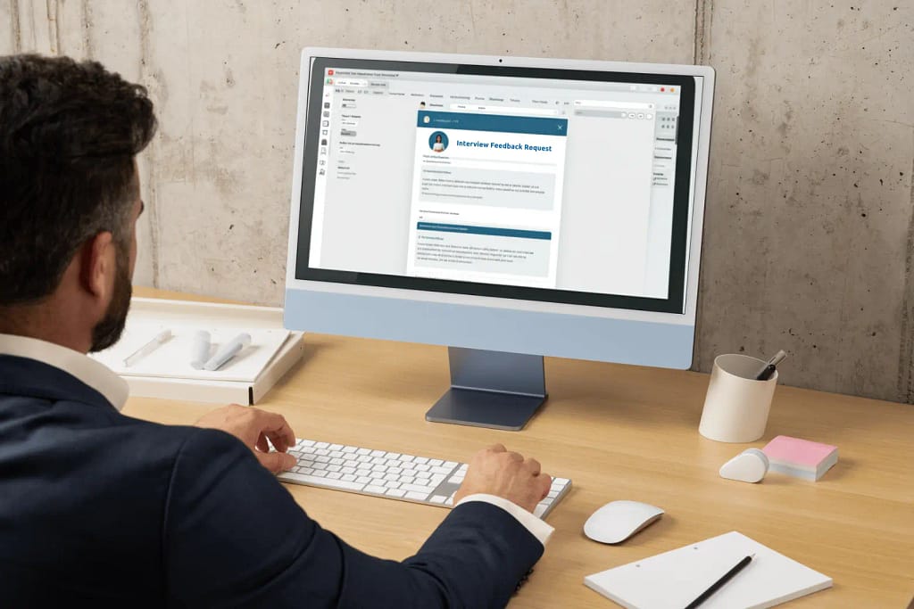 A man in a suit reviewing an email on his desktop screen labeled “Interview Feedback Request”